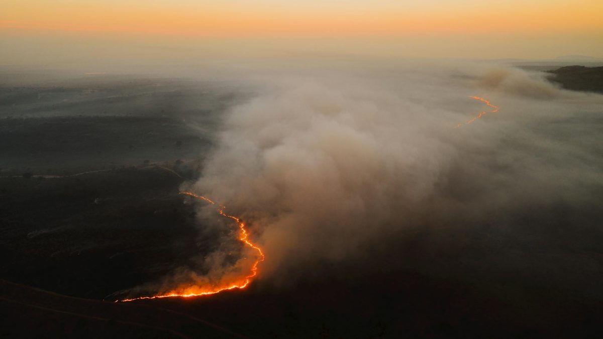 Dramatic aerial shot of a forest fire spreading with smoke at sunset in South Africa.